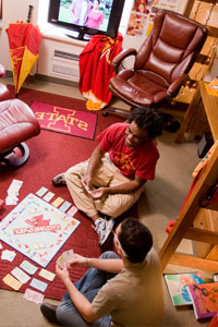 Students sit around a game board playing. 