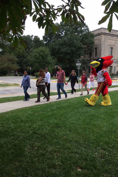 Iowa State University Mascot Cy walking beside students on sidewalk. 