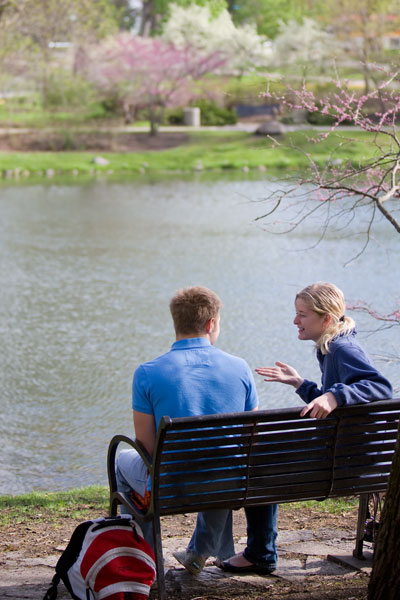 Two students sit on park bench in front of Lake Laverne on Iowa State University Campus.