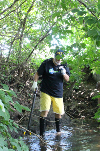Volunteer with mud boots on walking in College Creek on Iowa State University's campus.